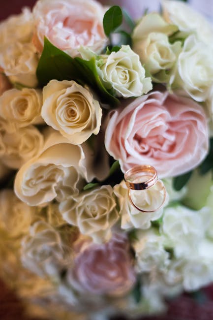 A close-up image of a bouquet featuring soft pink and creamy white roses, arranged with lush green leaves. The roses display delicate, velvety petals with some in full bloom and others partially close
